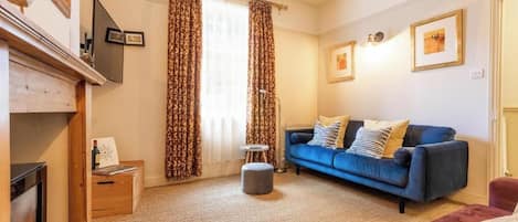 A living room with a blue sofa, a fireplace, and a large window with curtains.