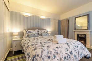 Een hotelkamer met een groot bed, een nachtkastje met een lamp, een spiegel en een open haard.