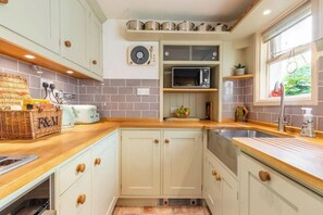 Een keuken met witte kastjes, een magnetron en een raam met uitzicht.