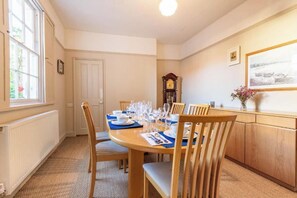 Een eethoek met een ronde tafel voor vier personen, houten stoelen, een klok aan de muur en een raam met uitzicht.