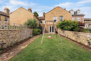 Una propiedad residencial con un muro de piedra, un patio con césped y un columpio de madera.