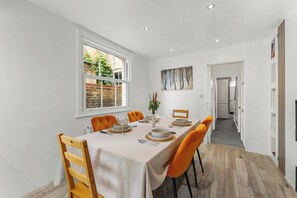 Un comedor con una mesa dispuesta para cuatro, una ventana y un pasillo que conduce a otras habitaciones.