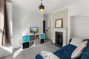 Una sala de estar con chimenea, televisor sobre un mueble bajo y sofá azul.