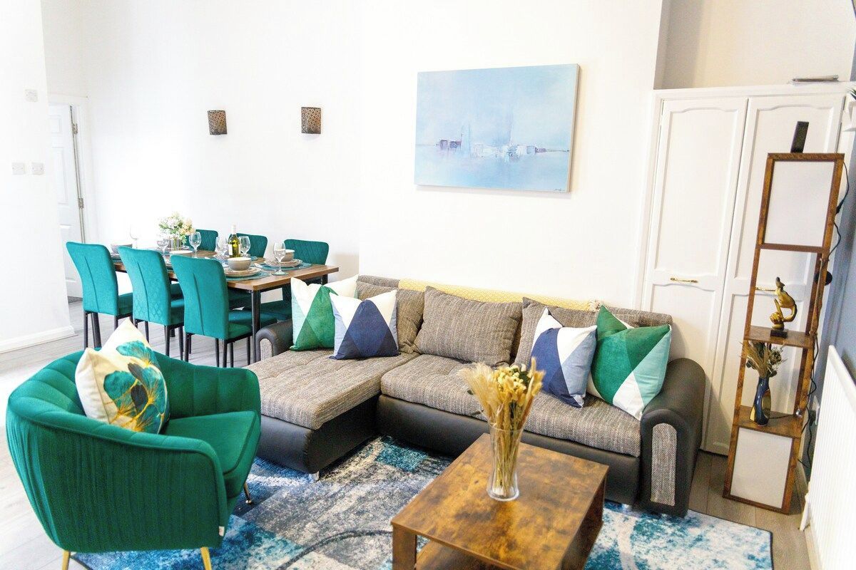 A living room with a sectional sofa, teal chairs, a coffee table, and a painting on the wall.