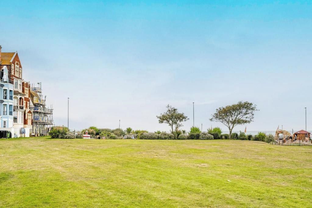 A grassy field with a row of buildings on the left, including one under construction.