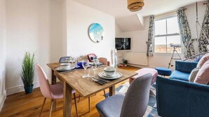 A dining area with a wooden table set for four, a potted plant, and a blue sofa in the background. - Modern Cromer Coastal Flat (Norfolk)