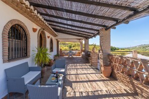 A covered outdoor seating area with wicker furniture, potted plants, and a view of the countryside. - Villa Rosafina - Three Bedroom Villa, Sleeps 6 (Frigiliana)