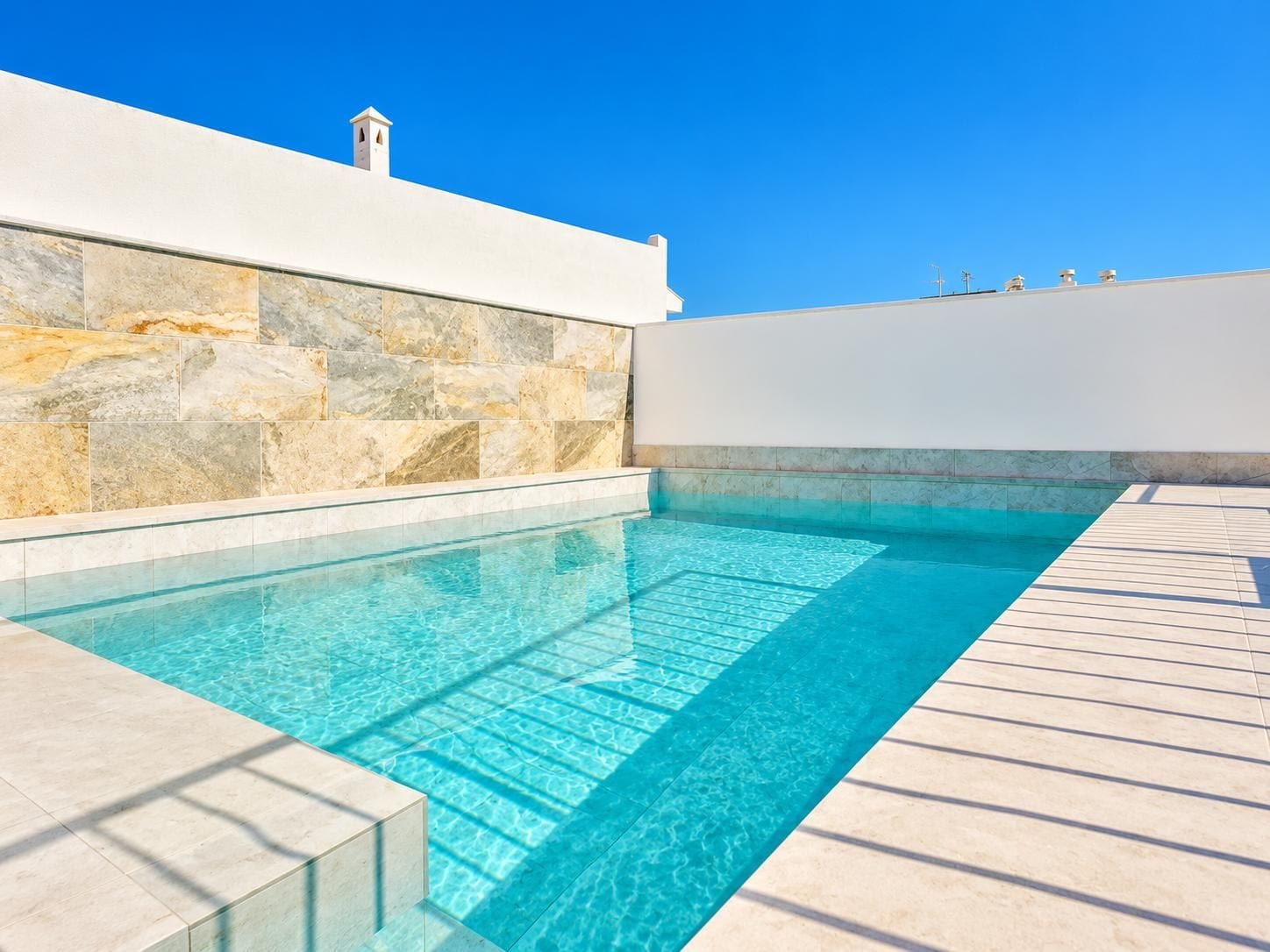 Une piscine à l’eau d’un bleu cristallin, entourée de murs en pierre et dotée d’une terrasse en bois.