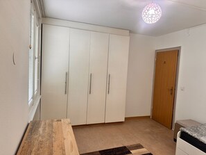 Ett sovrum med en garderob, ett nattduksbord, en säng, en dörr och en hängande lampa.