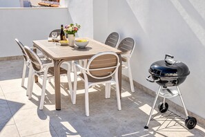 Eine Terrasse im Freien mit Tisch, Stühlen, einem Grill und einem Blumenvasen.