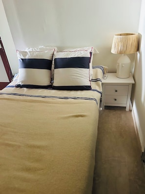 A bed with striped bedding, a bedside table with a lamp, and a nightstand with a phone. - The Open Sea (Cassis)