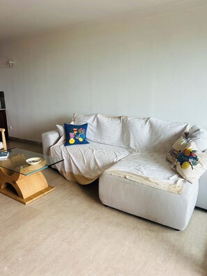 A white sofa with patterned cushions, a glass coffee table with a bowl, and a wooden side table. - The Open Sea (Cassis)