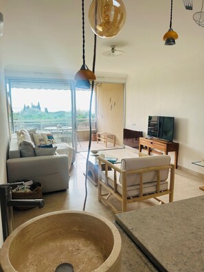 A modern living room with a sofa, dining table, and chairs, a television, and a view through a glass door. - The Open Sea (Cassis)