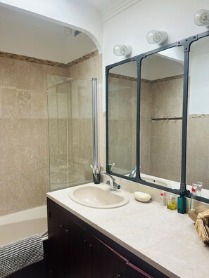 A bathroom with a glass shower enclosure, a sink with a mirror, and toiletries on the counter. - The Open Sea (Cassis)