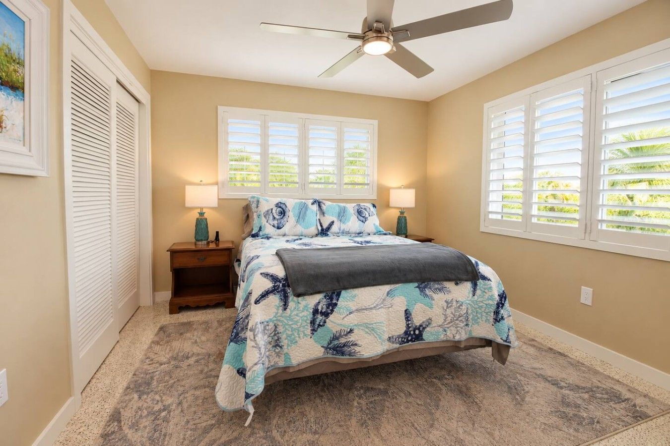 A bedroom with a bed, two bedside lamps, a ceiling fan, and a window with blinds.