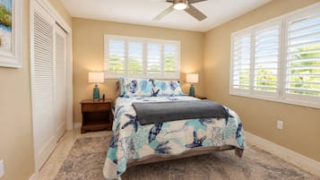 A bedroom with a bed, two bedside lamps, a ceiling fan, and a window with blinds.