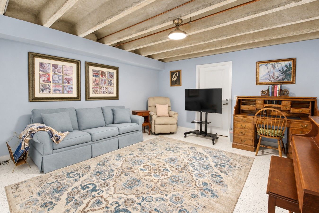 A living room with a sofa, armchair, TV, wooden desk, and a patterned rug.