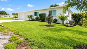 A single-story house with a well-maintained lawn and several small trees. - Jensen Beach 3BR/3BA Family Retreat + Game Room (Jensen Beach)