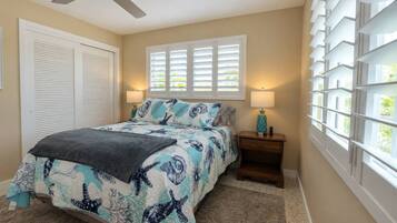 A bedroom with a bed, a ceiling fan, a window with blinds, and a nightstand with a lamp.