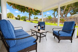 A covered patio with two blue cushioned chairs and a table, a bottle of red wine, and glasses on the table. - Beach Days, Game Nights Near Downtown Jensen Beach (Jensen Beach)