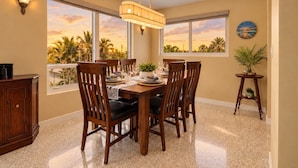 A dining area with a table set for six, surrounded by chairs, with a view of palm trees through large windows. - Jensen Beach 3BR/3BA Family Retreat + Game Room (Jensen Beach)