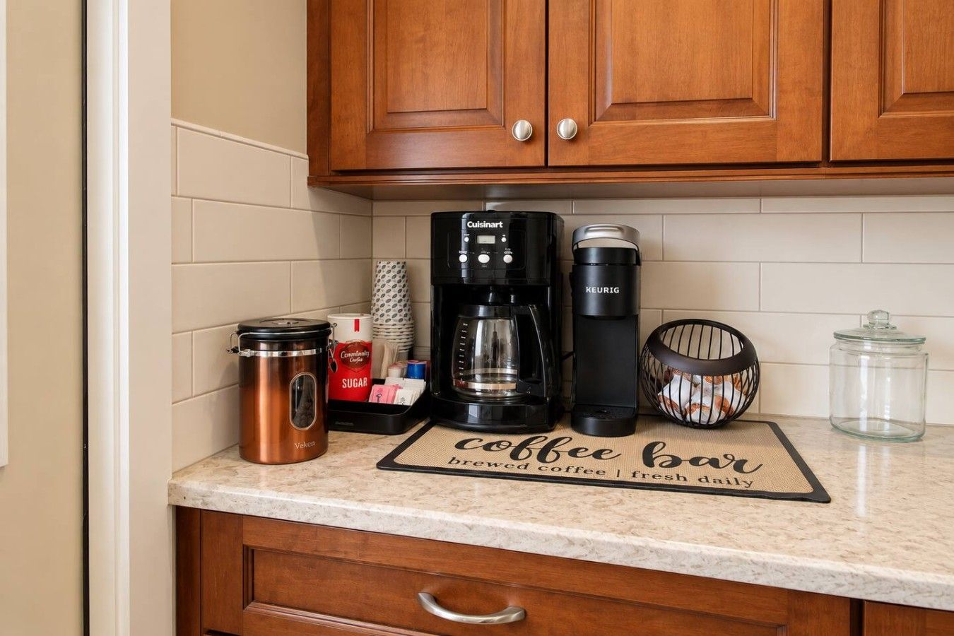 A kitchen counter with a coffee maker, a kettle, a sugar container, and a coffee mug.