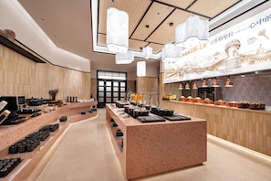 A modern restaurant interior with a central serving counter, multiple seating areas, and a decorative wall with a mountain illustration. - LIAN HOTEL (Deqin)
