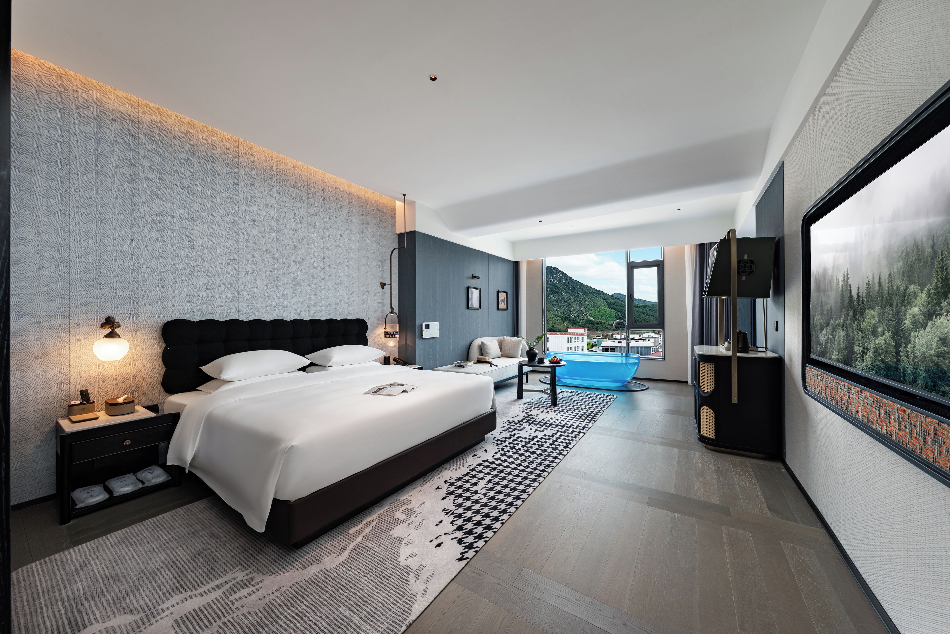 A modern hotel room with a large bed, a sitting area, and a view of a mountainous landscape.