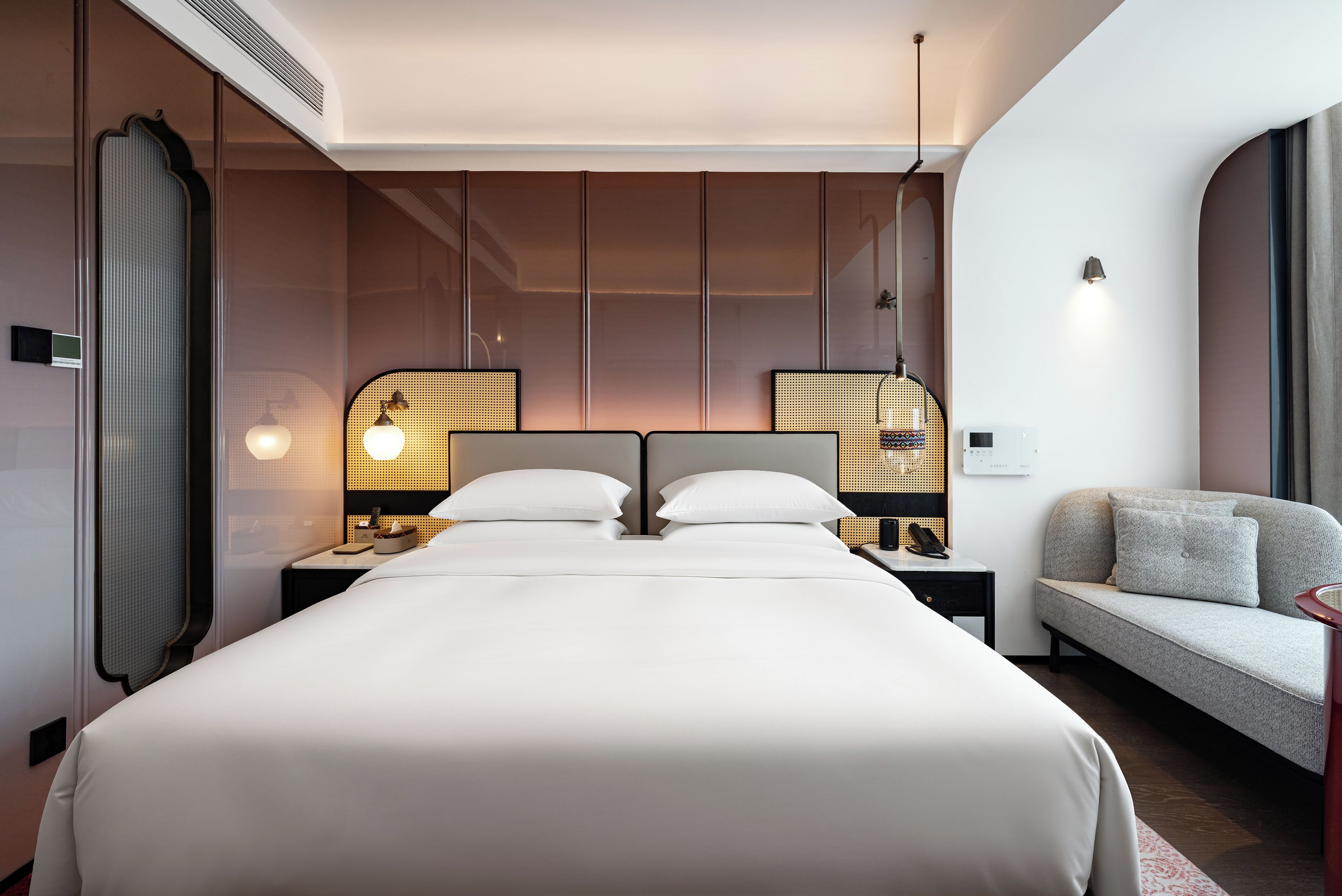 A hotel room with a large bed, two bedside tables, a sofa, and a wall-mounted lamp.