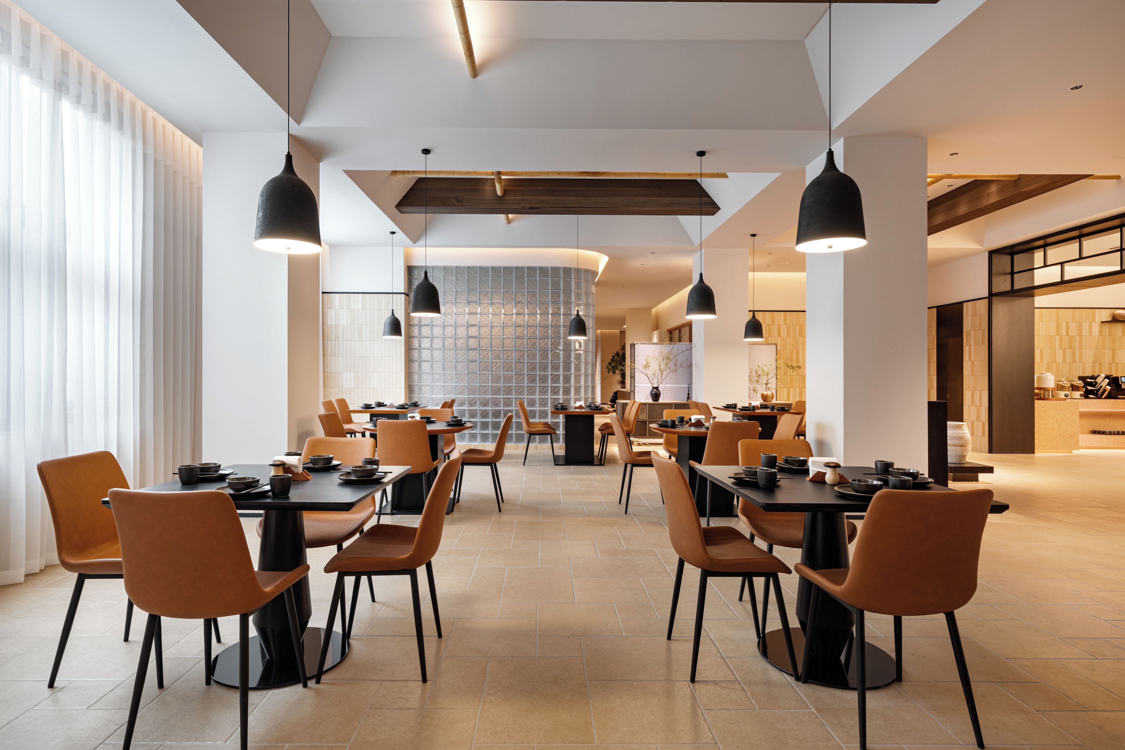A modern dining area with multiple tables and chairs, a high ceiling with exposed beams, and pendant lighting.