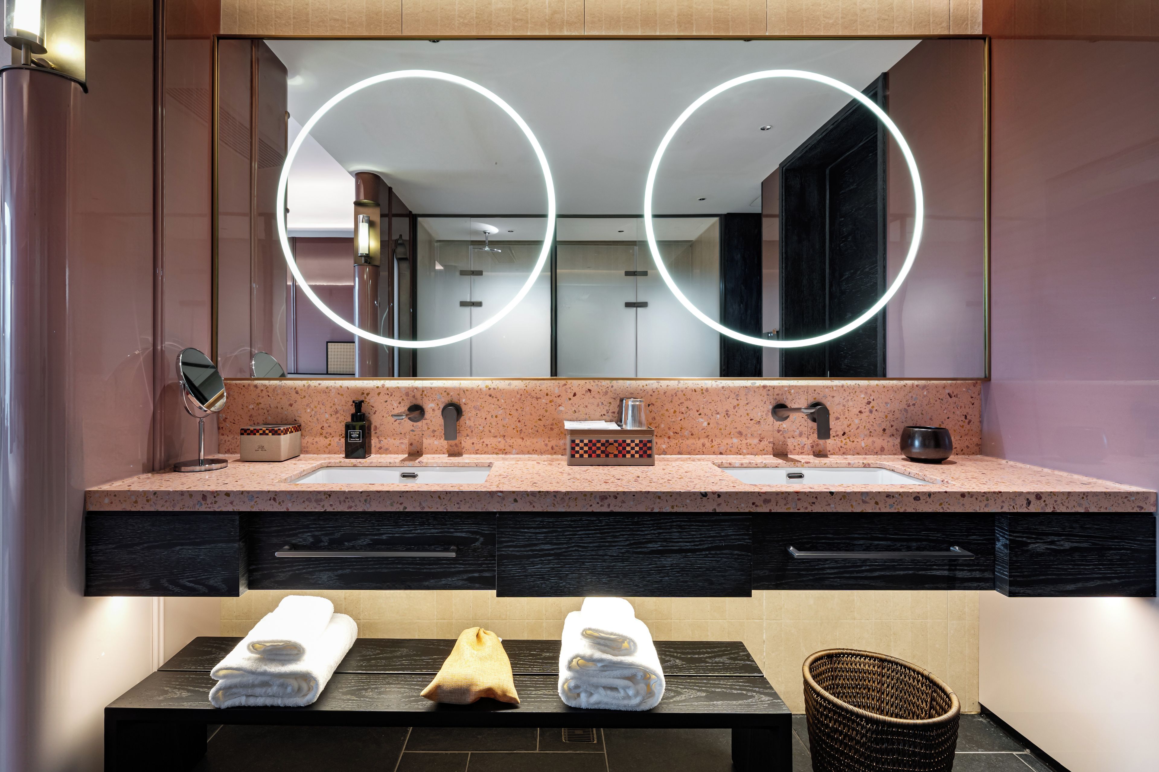 A modern bathroom with a double sink vanity, a large mirror with circular lighting, and two towels on the counter.