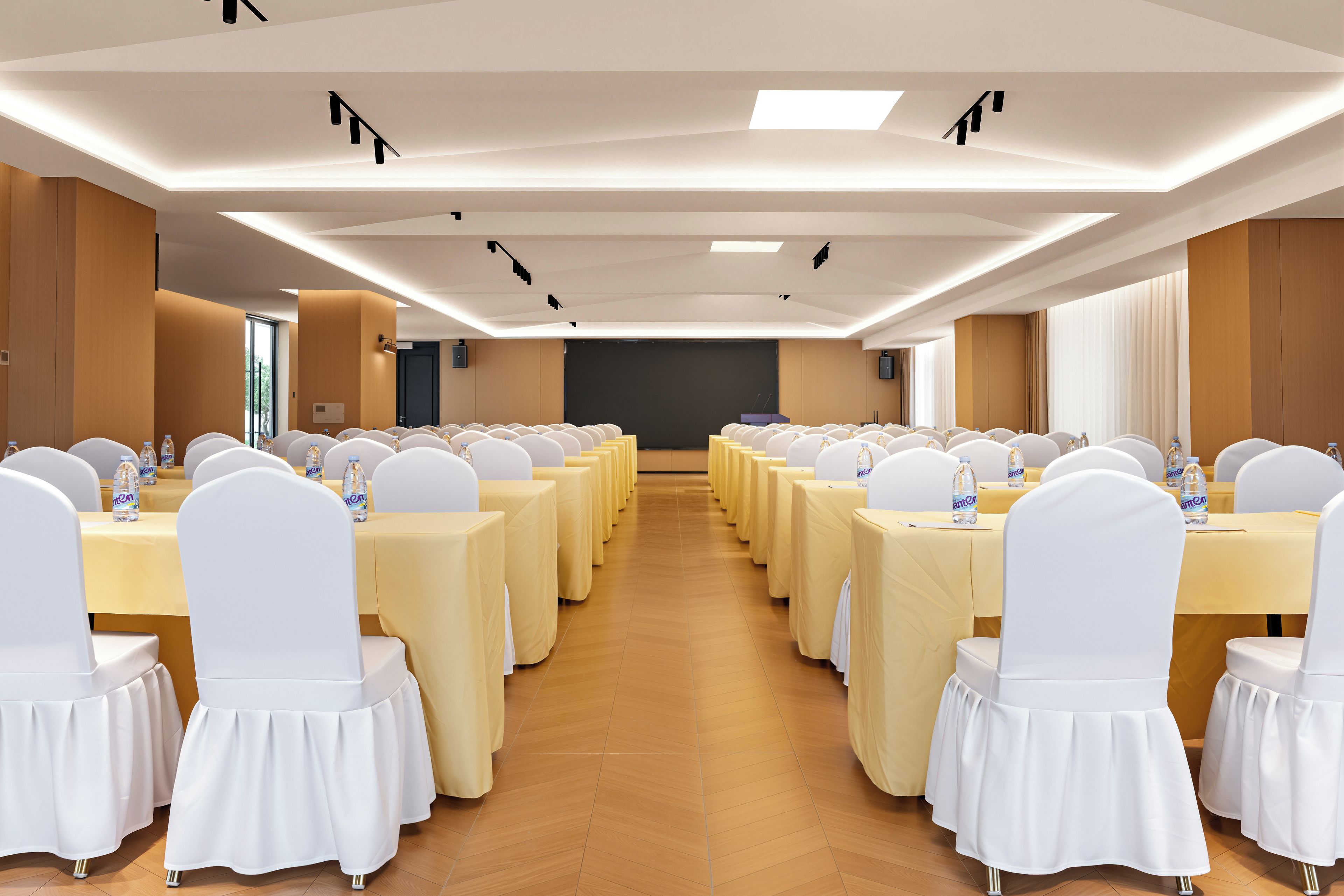 Un salón de conferencias con filas de mesas, sillas y una pantalla para proyector.