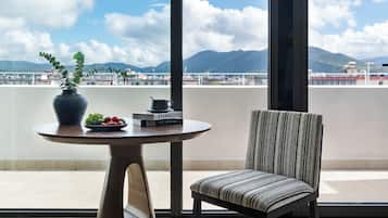 A balcony with a round table, a chair, a potted plant, and a view of mountains and buildings.