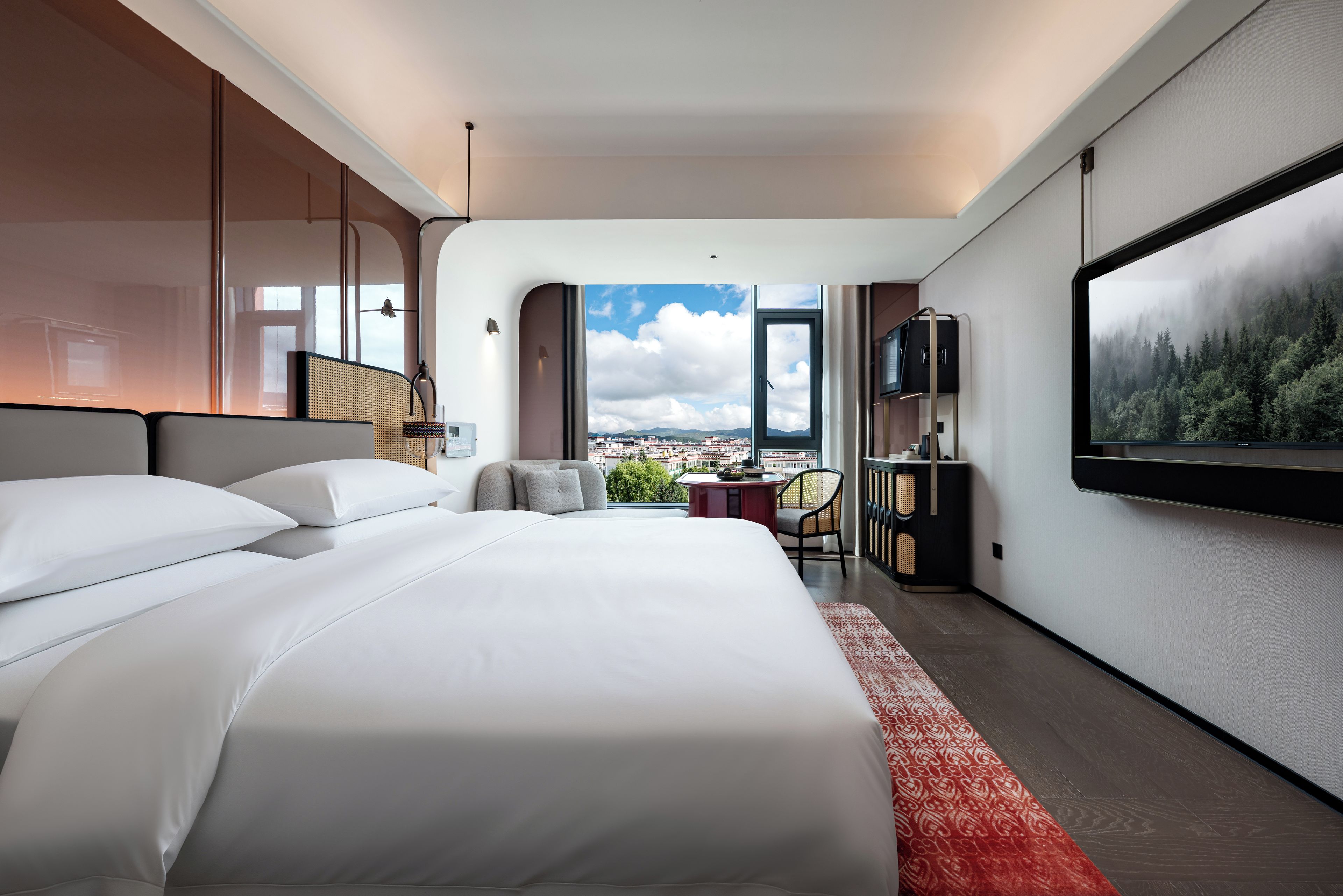 A hotel room with a large bed, a desk, a chair, a TV, and a view of the city.