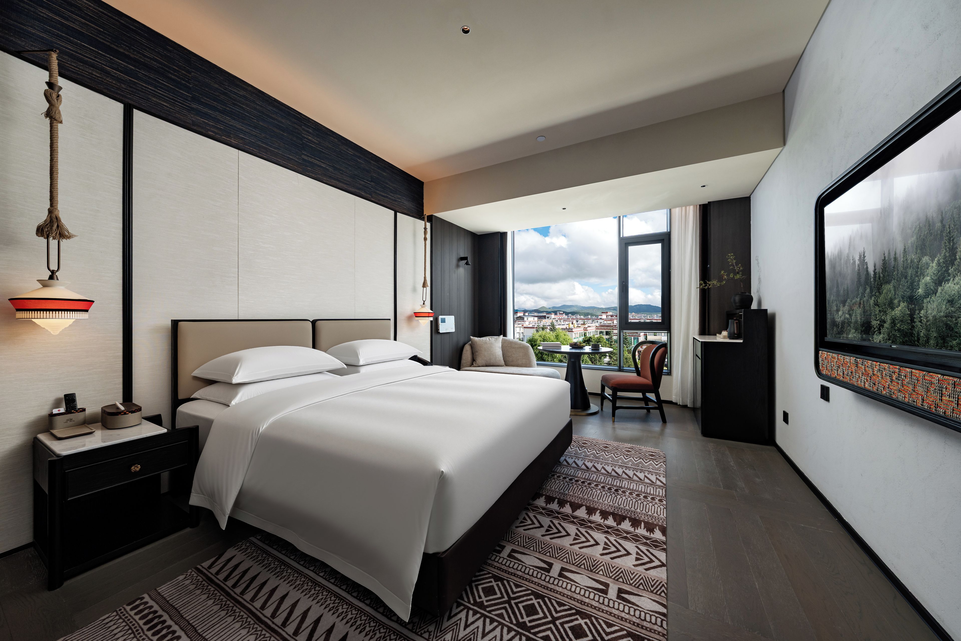 Una habitación de hotel moderna con una cama grande, un escritorio, una silla y vistas de la ciudad a través de amplias ventanas.