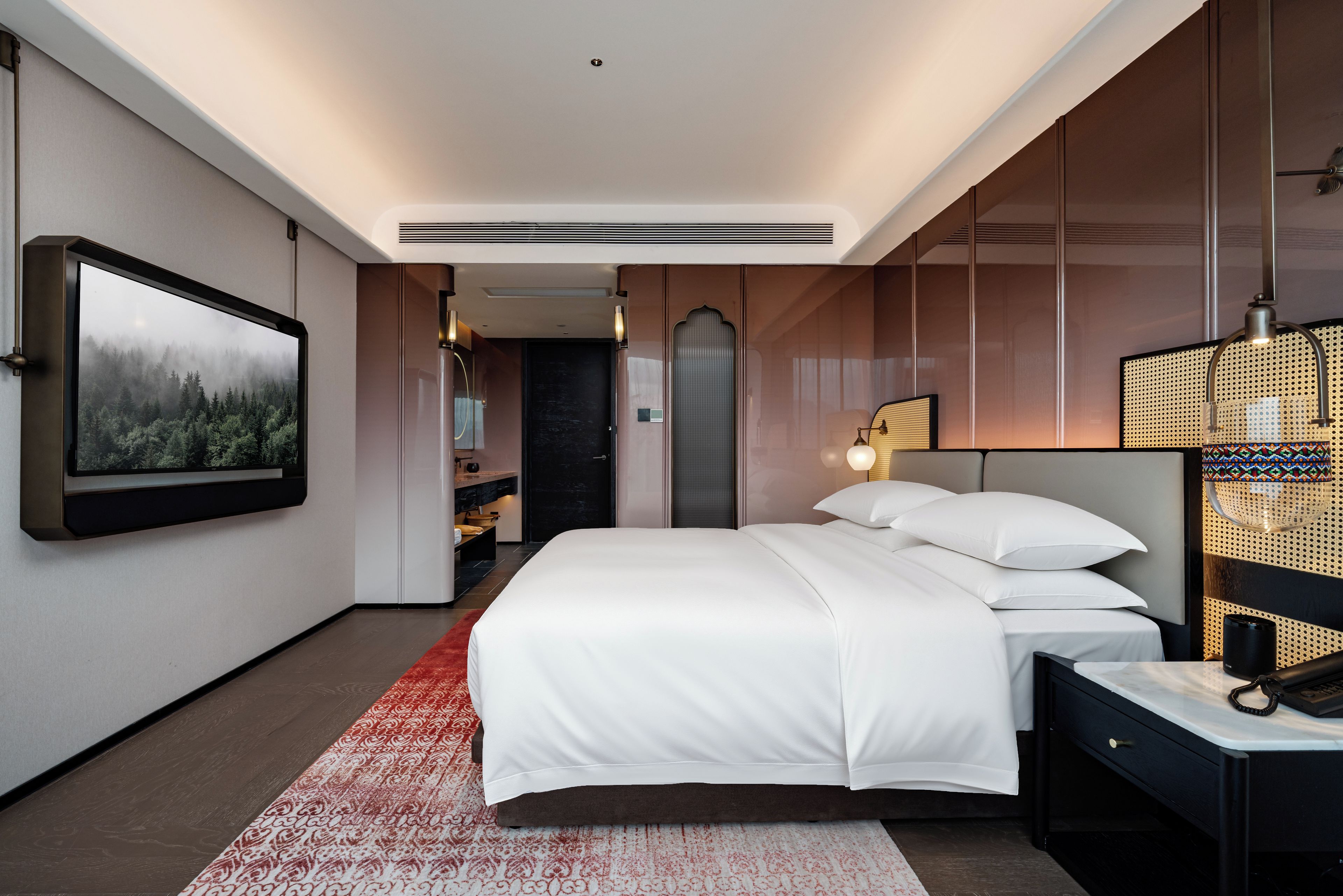 A modern hotel room with a large bed, a television mounted on the wall, and a red patterned rug.