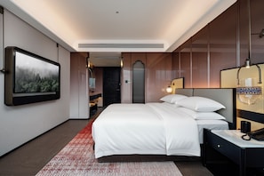 A modern hotel room with a large bed, a television mounted on the wall, and a red patterned rug. - LIAN HOTEL (Deqin)
