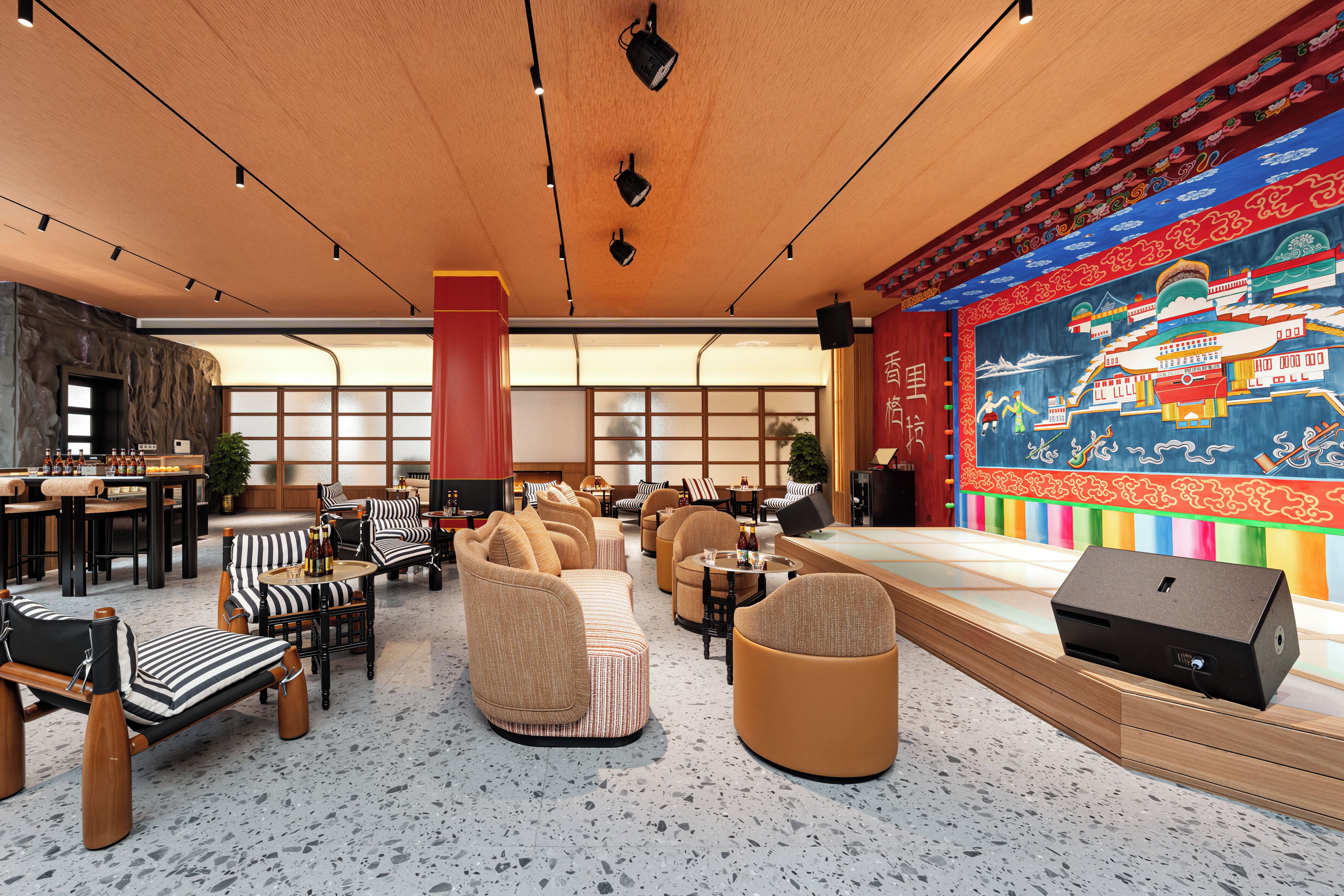 A spacious lounge area with seating arrangements, a stage, and a large wall mural.