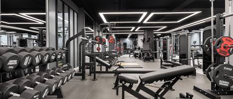 A gym with weightlifting equipment, benches, and a mirrored wall.