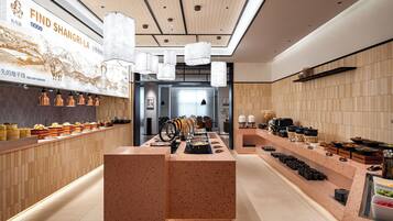A modern restaurant interior with a central serving counter, multiple hanging pendant lights, and a variety of dishes displayed on the counter.