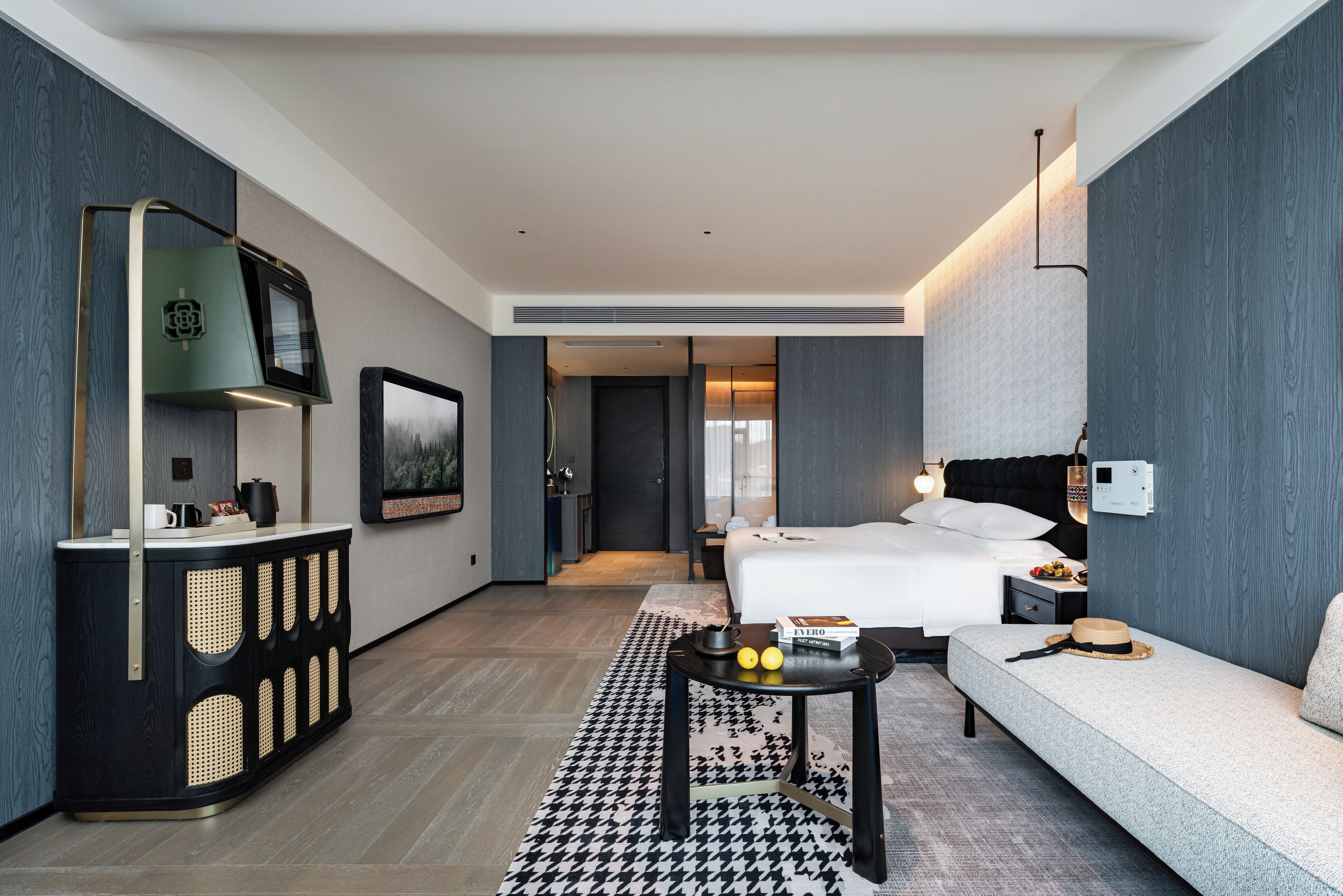 A modern hotel room with a bed, a sofa, a small table, and a TV.