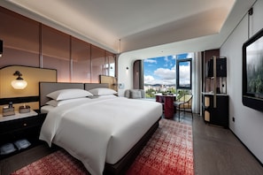 A modern hotel room with a large bed, a desk, a chair, a TV, and a balcony with a city view. - LIAN HOTEL (Deqin)
