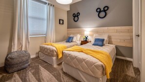 Hotellihuone, jossa on kaksi sänkyä, sängynpääty, ikkuna verhoilla, seinään kiinnitetty valaisin ja pieni yöpöytä.