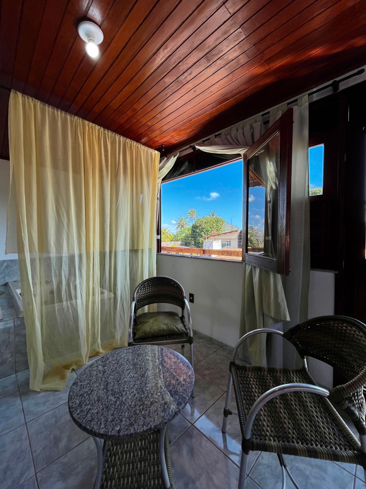 Un balcón con dos sillas de mimbre, una mesita redonda y vistas a una zona residencial.