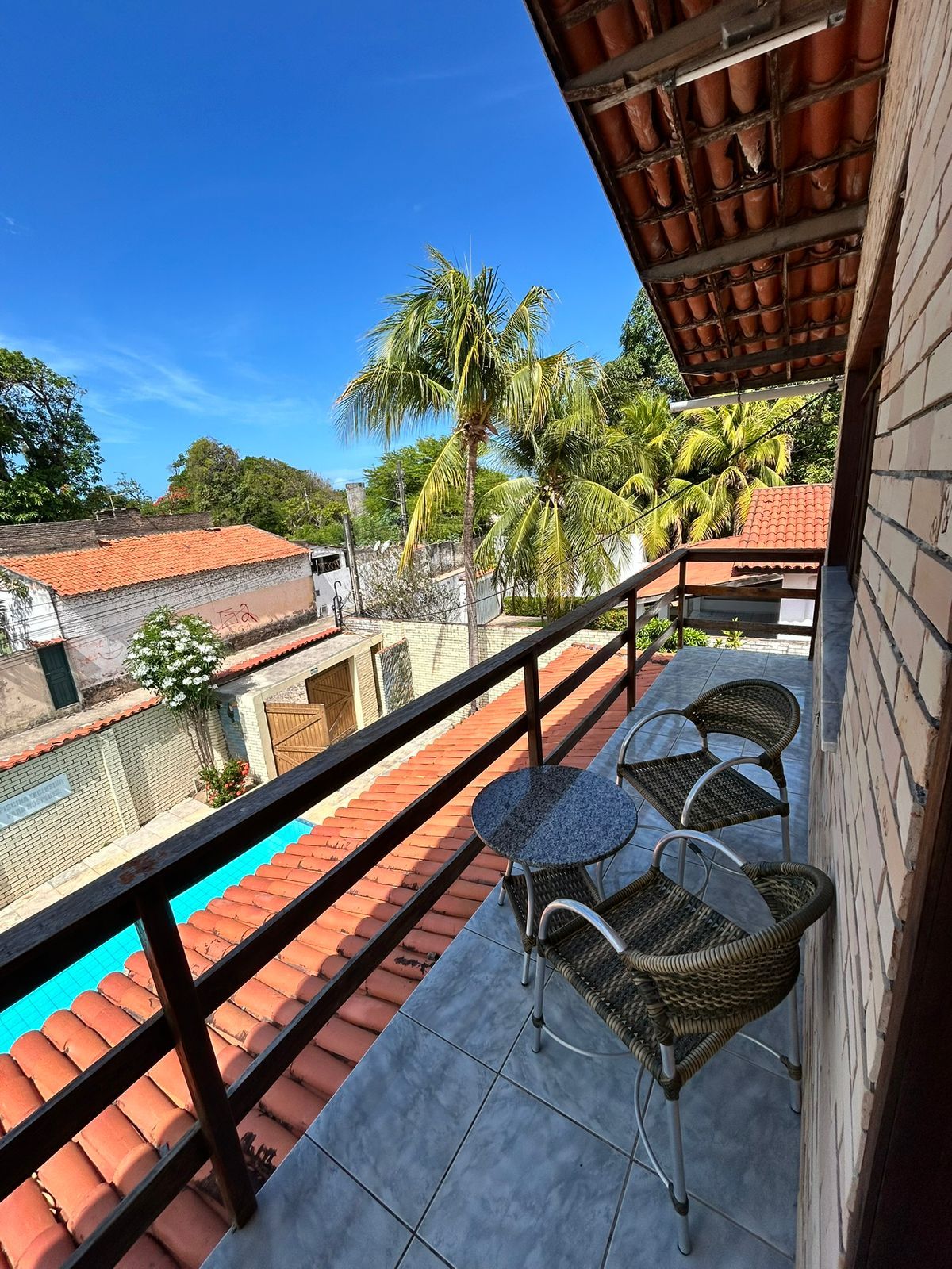 Un balcón con piscina, mobiliario de mimbre y vistas al vecindario.