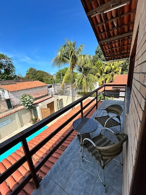 A balcony with a pool, wicker furniture, and a view of the neighborhood.