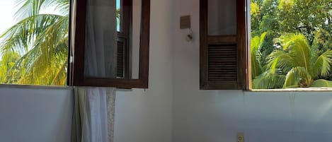 Een kamer met een bed, een bankje en ramen met uitzicht op groen.