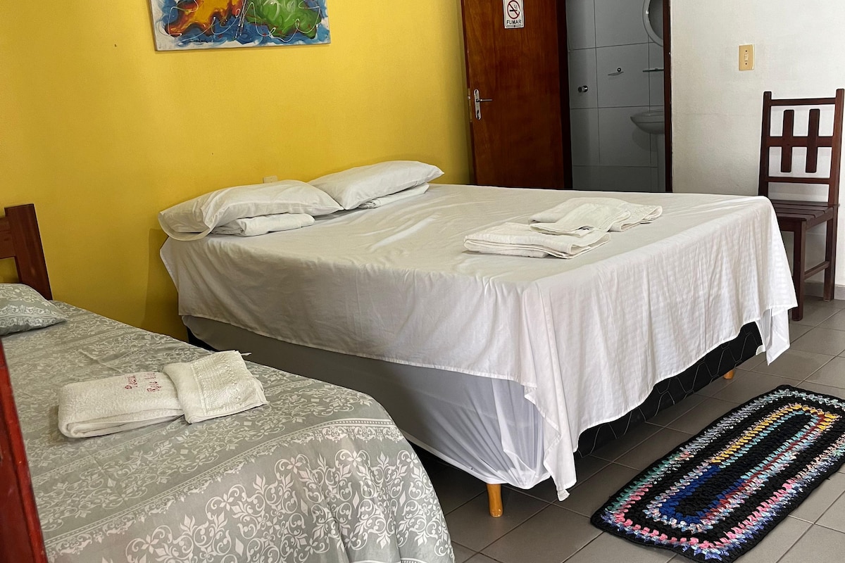 A room with two beds, a door, a chair, and a colorful painting on the wall.