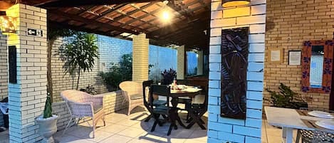 Een terras met overdekte zithoek, een tafel en potplanten.