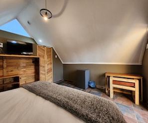 Un dormitorio con techo inclinado, una cama, un televisor y una pequeña mesa.